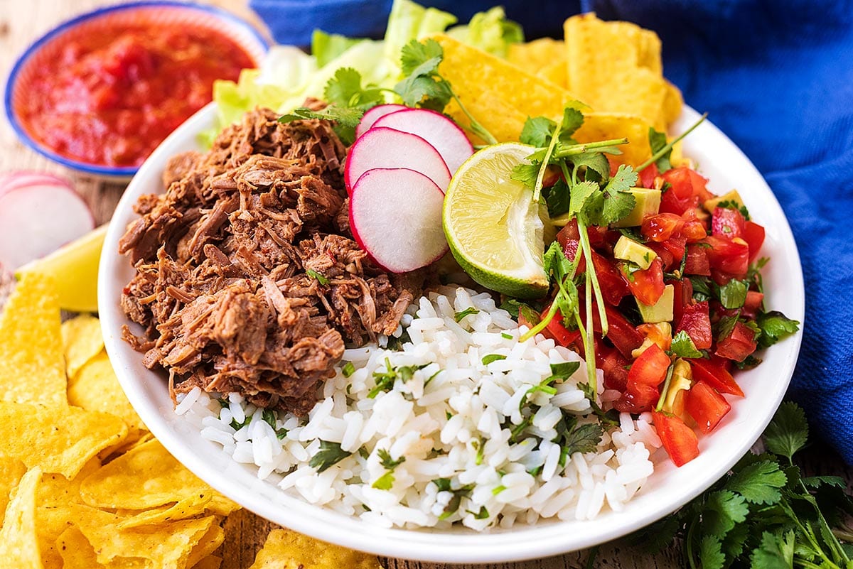 A burrito bowl containing meat, rice, salad and herbs