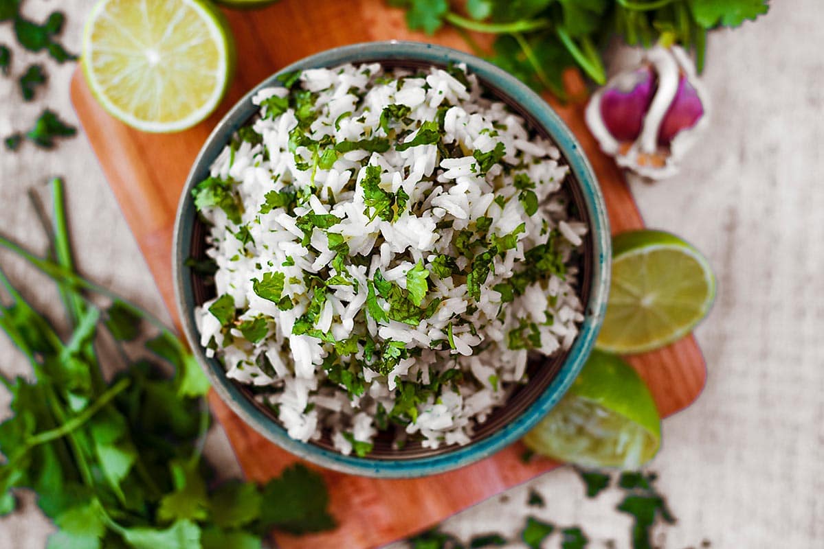 A bowl of cilantro lime rice next to coriander leaves and limes