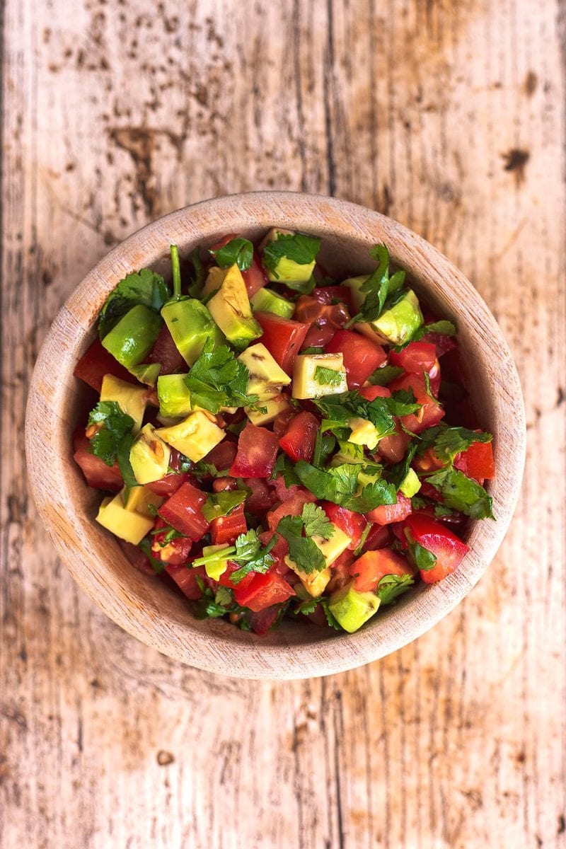 A small wooden bowl containing chopped tomato and avocado salsa