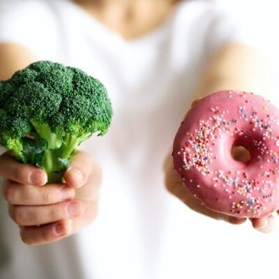 Young woman in white T-shirt choosing between broccoli or junk food, donut. Healthy clean detox